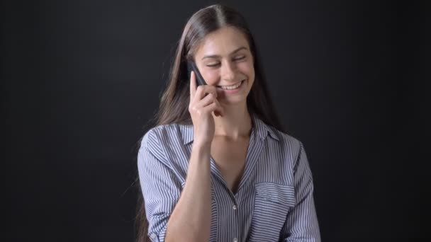 Charming happy young woman talking on phone and smiling, standing isolated on black background - Video, Çekim