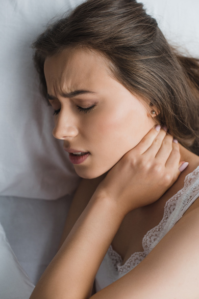Genç kadın yatakta yatan süre boyun ağrısı muzdarip üstten görünüm - Fotoğraf, Görsel