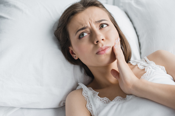 attraente giovane donna che soffre di mal di denti e guardando lontano mentre si trova a letto
  - Foto, immagini