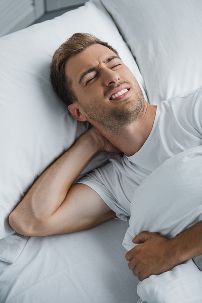 young man lying in bed and suffering from pain in neck  - Photo, Image