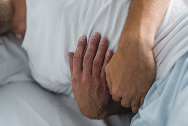 close-up partial view of man suffering from stomach pain in bed  - Photo, Image
