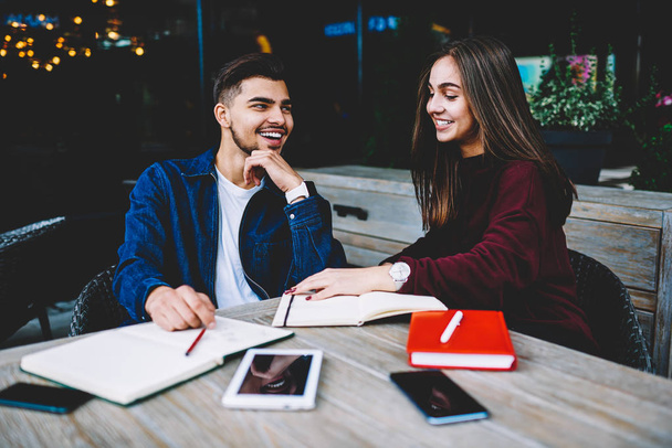 Happy male and female students smiling cheerfully while having friendly conversation, cheerful best friends working on common projects sitting on cafe terrace joking and laughing during discussion - Zdjęcie, obraz