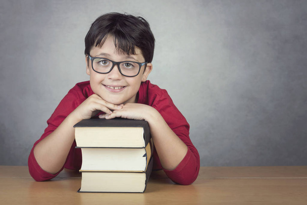 smiling little boy leaning on books on a table on black background - Фото, изображение