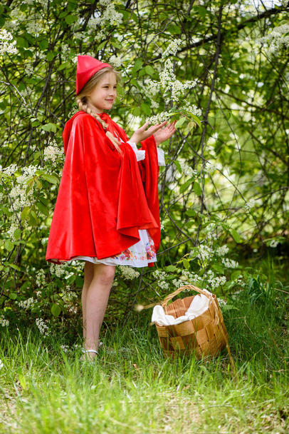 Sonriente rubia posando en un vestido de capucha roja cerca de árboles verdes
 - Foto, Imagen