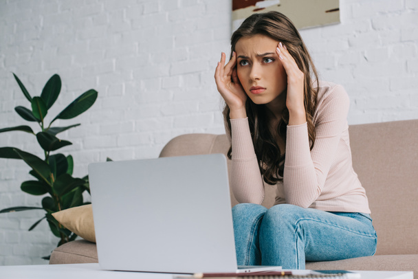 young woman with headache looking away while working with laptop at home - Photo, Image
