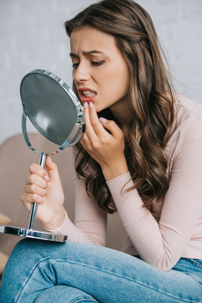 attractive young woman with tooth pain sitting and looking at mirror - Fotó, kép