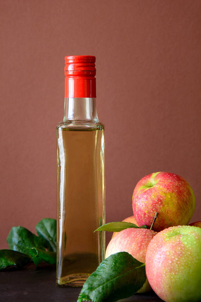 Apple vinegar in glass bottle and fresh apples on brown wooden desk - Fotografie, Obrázek