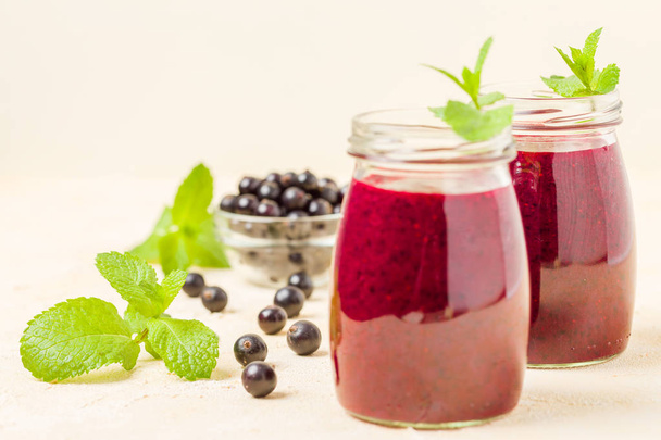 Currant smoothie decorated with fresh green mint leaves and raw ripe berries on yellow pastel background - transparent jars of summer blended vitamin cocktail for healthy food concept. - Фото, зображення
