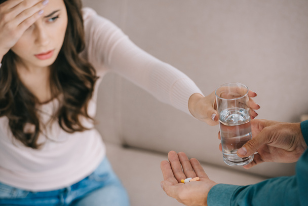 cropped shot of man giving glass of water and pills to woman suffering from headache - Фото, зображення