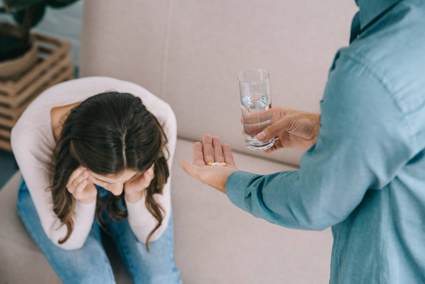 colpo ritagliato di uomo in possesso di vetro di acqua e pillole mentre la donna soffre di mal di testa
  - Foto, immagini