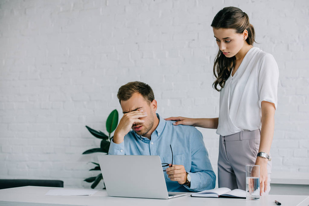 young woman looking at male colleague suffering from headache at workplace - Фото, зображення