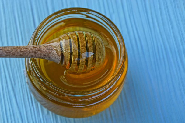 Wooden brown spoon in a glass jar of honey on a blue table - Фото, изображение
