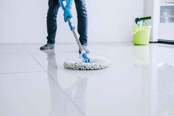 Husband housekeeping and cleaning concept, Happy young man in blue rubber gloves wiping dust using mop while cleaning on floor at home. - Фото, зображення