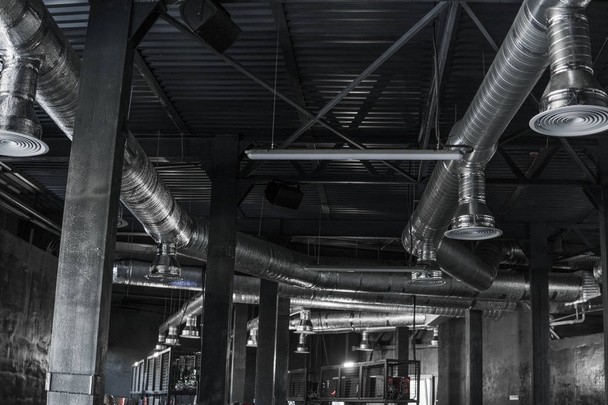 Büyük binaların tavanındaki havalandırma sistemi. Yeni binanın tavanından sarkan gümüş yalıtım malzemelerindeki havalandırma boruları.. - Fotoğraf, Görsel