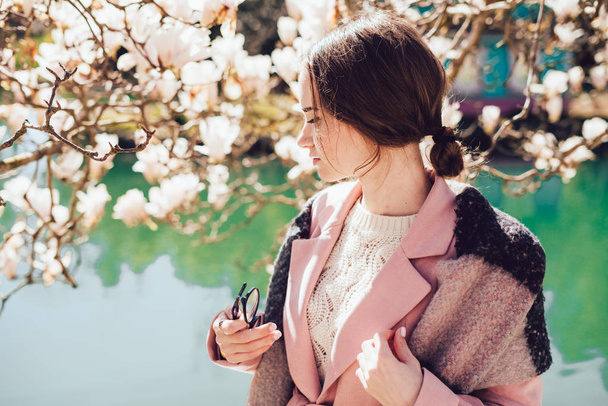 confident beautiful girl in a fashionable pink jacket posing by a pond in the park - Foto, imagen