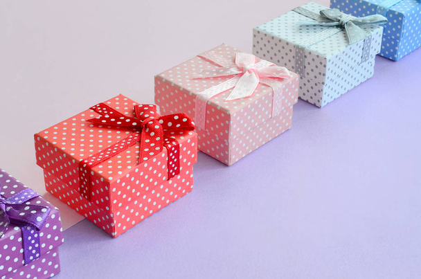 Small gift boxes of different colors with ribbons lies on a violet and pink color background. - Photo, Image