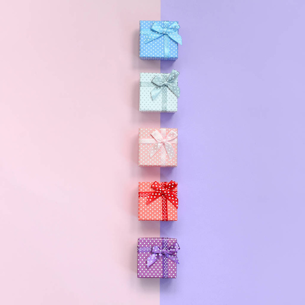 Pequeñas cajas de regalo de diferentes colores con cintas se encuentra en un fondo de color violeta y rosa
. - Foto, imagen