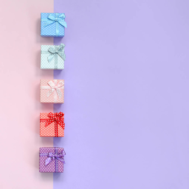 Невеликі подарункові коробки різних кольорів зі стрічками лежать на фіолетовому і рожевому кольоровому фоні
. - Фото, зображення