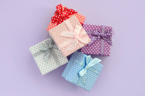 Σωρός από ένα μικρό χρωματισμένα κιβώτια δώρων με κορδέλες βρίσκεται σε μοβ φόντο. Μινιμαλισμός επίπεδη θέσει το top view. - Φωτογραφία, εικόνα