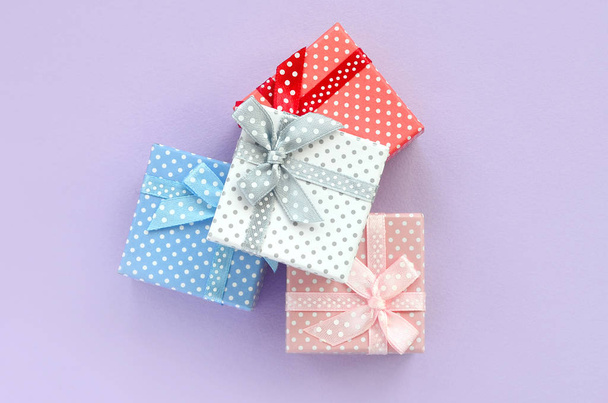 Il mucchio di piccole scatole di regalo colorate con nastri si trova su uno sfondo viola. Minimalismo piatto lay vista dall'alto
. - Foto, immagini