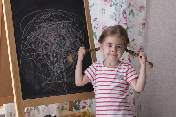 Παιδί πλησιάζει με τα κομμάτια του χρώματος κιμωλία στον πίνακα κιμωλίας. Το κορίτσι έκφραση της δημιουργικότητας και εξετάζοντας τη φωτογραφική μηχανή. Έννοια της έκφρασης και μάθησης - Φωτογραφία, εικόνα