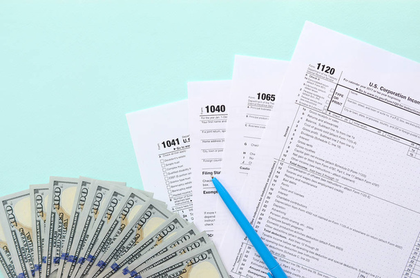Les formulaires fiscaux se trouvent près de cent billets de dollars et stylo bleu sur un fond bleu clair. Déclaration de revenus
. - Photo, image