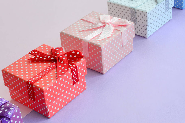 Petites boîtes-cadeaux de différentes couleurs avec des rubans repose sur un fond de couleur violette et rose
. - Photo, image