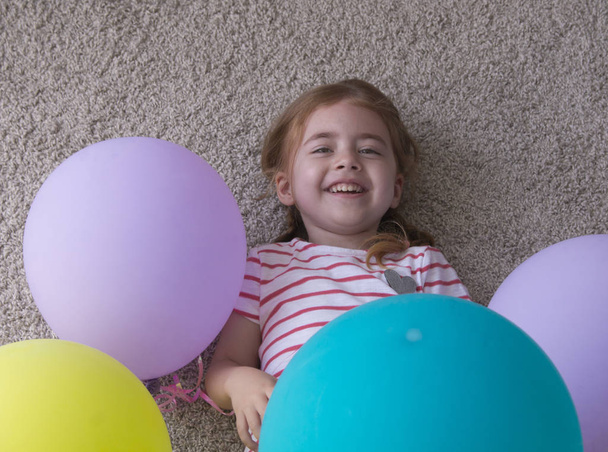девочка с шариками, ребенок с шариками, ребенок с шариками, лежащими на полу. Девушка выражает творчество, смотрит в камеру и улыбается.
. - Фото, изображение