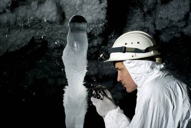 speleolog w jaskini bada olbrzymi Lodowy stalagmit pokryte szronu, na tle ciemnej skały pokryte kryształkami lodu - Zdjęcie, obraz