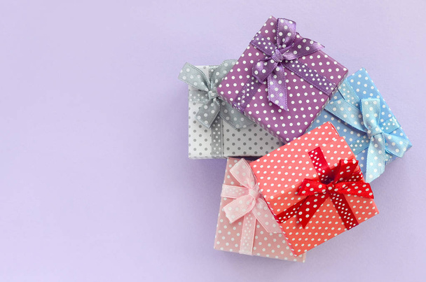 Auf violettem Hintergrund liegt ein Stapel kleiner farbiger Geschenkboxen mit Schleifen. Minimalismus flach von oben. - Foto, Bild