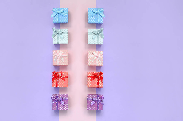 Pequeñas cajas de regalo de diferentes colores con cintas se encuentra en un fondo de color violeta y rosa
. - Foto, Imagen