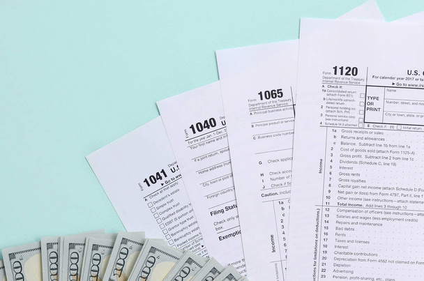 Formularios de impuestos se encuentra cerca de billetes de cien dólares y pluma azul sobre un fondo azul claro. Declaración del impuesto sobre la renta
. - Foto, imagen