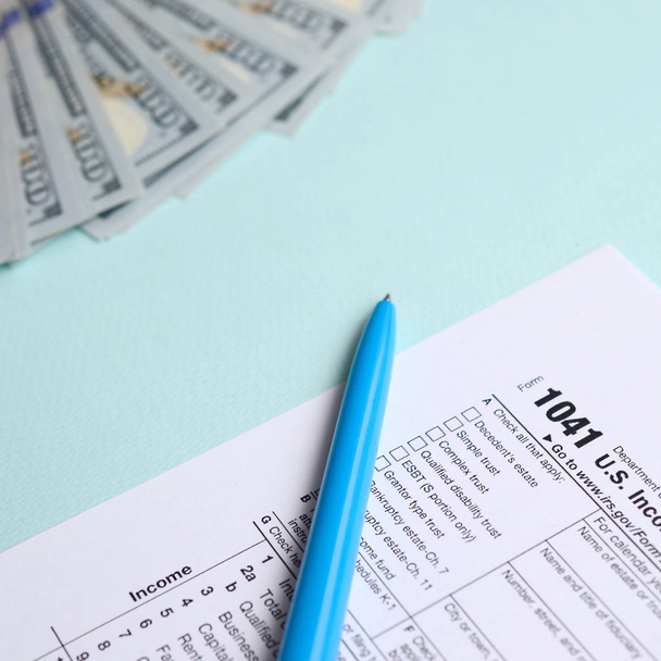 1041 belasting formulier ligt in de buurt van honderd dollarbiljetten en blauwe pen op een licht blauwe achtergrond. Ons inkomen belasting terugkeer van landgoederen en vertrouwensrelaties. - Foto, afbeelding