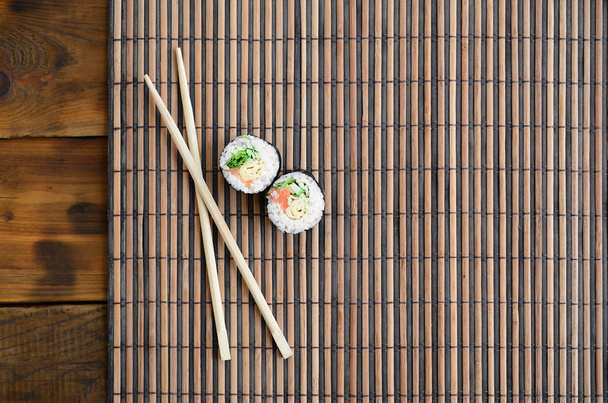 Sushi-Rollen und Holzstäbchen liegen auf einer Bambusstroh-Serviermatte. traditionelle asiatische Küche. Ansicht von oben. flacher Laien-Minimalismus mit Kopierraum. - Foto, Bild