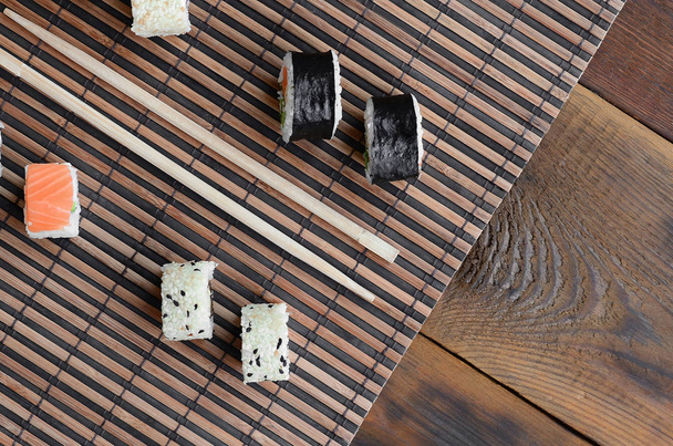 Sushi rolls and wooden chopsticks lie on a bamboo straw serwing mat. Traditional Asian food. Top view. - Photo, Image