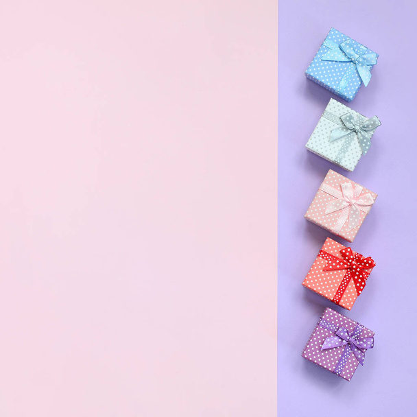 Μικρό δώρο κουτιά διαφόρων χρωμάτων με κορδέλες βρίσκεται σε χρώμα βιολετί και ροζ φόντο. - Φωτογραφία, εικόνα