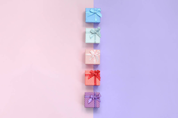 Маленькие подарочные коробочки разных цветов с лентами лежат на фиолетовом и розовом фоне
. - Фото, изображение
