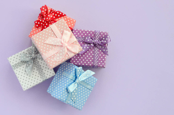 Pile of a small colored gift boxes with ribbons lies on a violet background. Minimalism flat lay top view. - Photo, Image