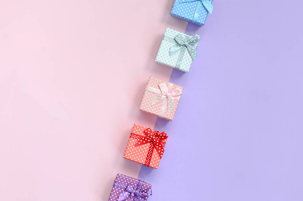 Small gift boxes of different colors with ribbons lies on a violet and pink color background. - Photo, Image