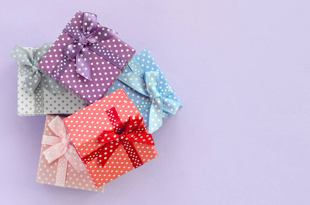 Σωρός από ένα μικρό χρωματισμένα κιβώτια δώρων με κορδέλες βρίσκεται σε μοβ φόντο. Μινιμαλισμός επίπεδη θέσει το top view. - Φωτογραφία, εικόνα