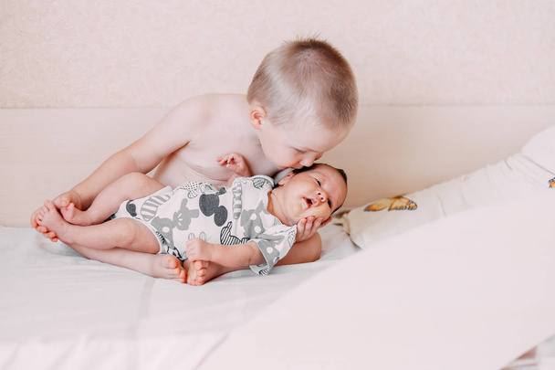 elder little blonde toddler brother boy holding his baby sister in his hands on bed at home family concept love - Photo, Image