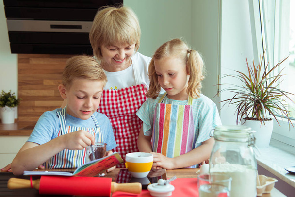 Счастливая бабушка с внуками, веселящимися во время выпечки кексов и печенья
 - Фото, изображение