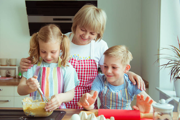 Happy grandmother with her grandchildren having fun during baking muffins and cookies - Фото, зображення