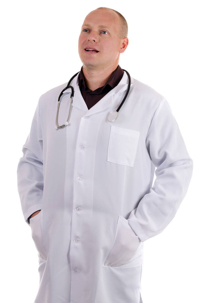 Médico adulto con bata blanca habla de la enfermedad mientras hace sus manos en bolsillos sobre fondo blanco
 - Foto, Imagen
