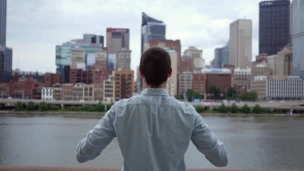 A man lifts his arms in a celebratory victory stance against cinematic skyline - Materiał filmowy, wideo