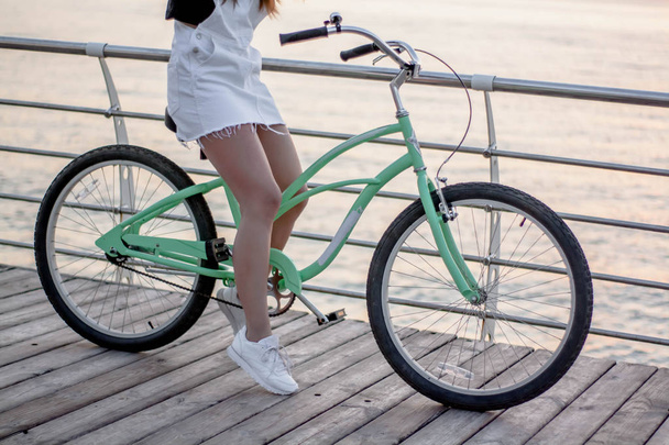 Закрытая, красивая молодая женщина с велосипедом, рулем, колесами, частью тела. Руки на руль.
 - Фото, изображение