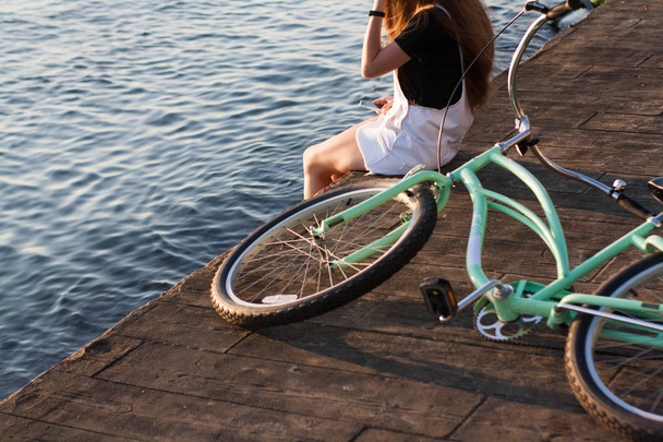 Закрытая, красивая молодая женщина с велосипедом, рулем, колесами, частью тела. Руки на руль.
 - Фото, изображение