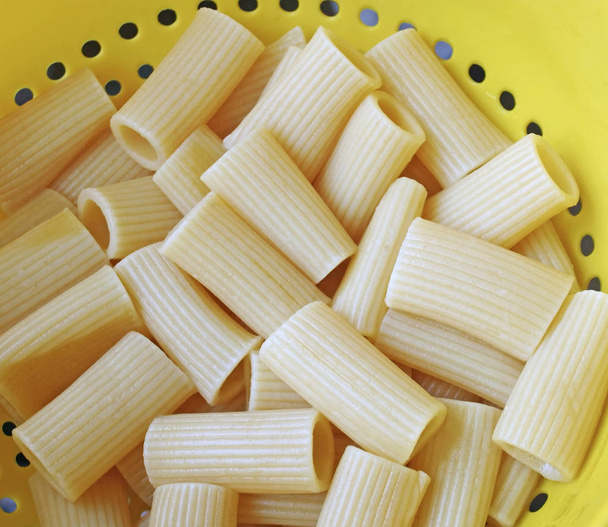 Pasta Rigatoni escurrida y cocida en un colador de plástico amarillo
 - Foto, imagen