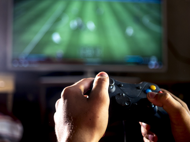 крупный план молодого человека с джойстиком для консоли, играющего в спортивный симулятор видеоигры на большом экране
 - Фото, изображение
