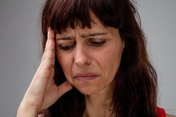 Malade femme avec un mal de tête migraine grimaçant comme elle tient sa main à son temple dans un plan rapproché de la tête recadrée
 - Photo, image